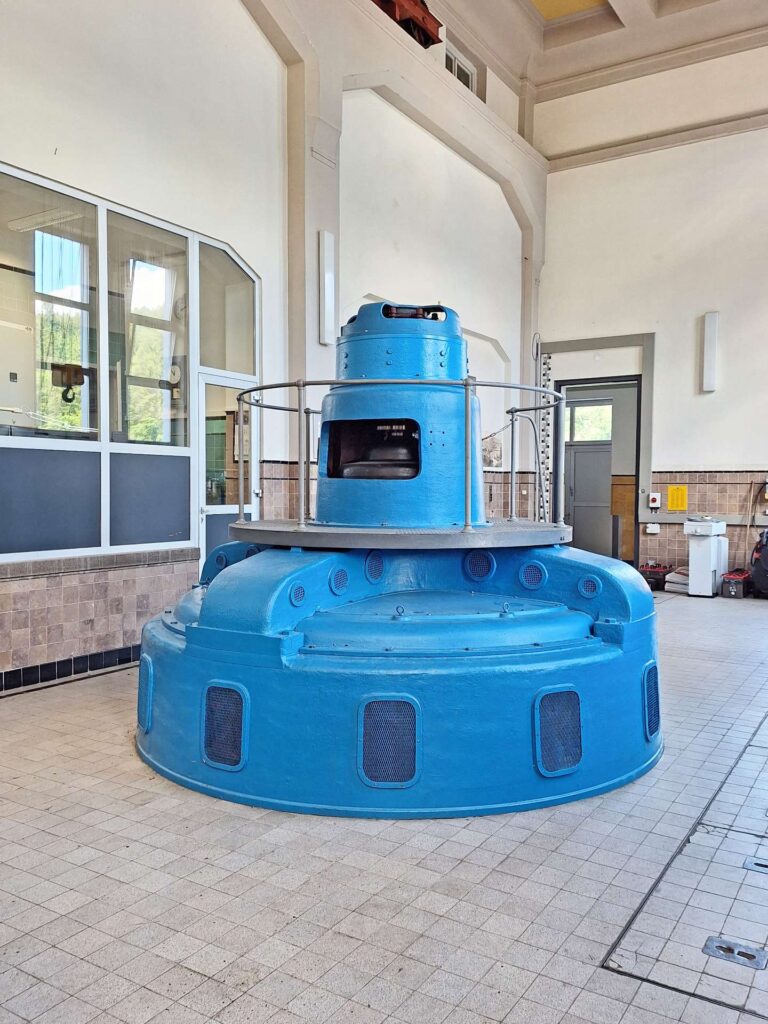 Blaue Turbine in der Maschinenhalle vom Kraftwerk Höllenstein, historische Industriearchitektur mit hellen Fliesen.