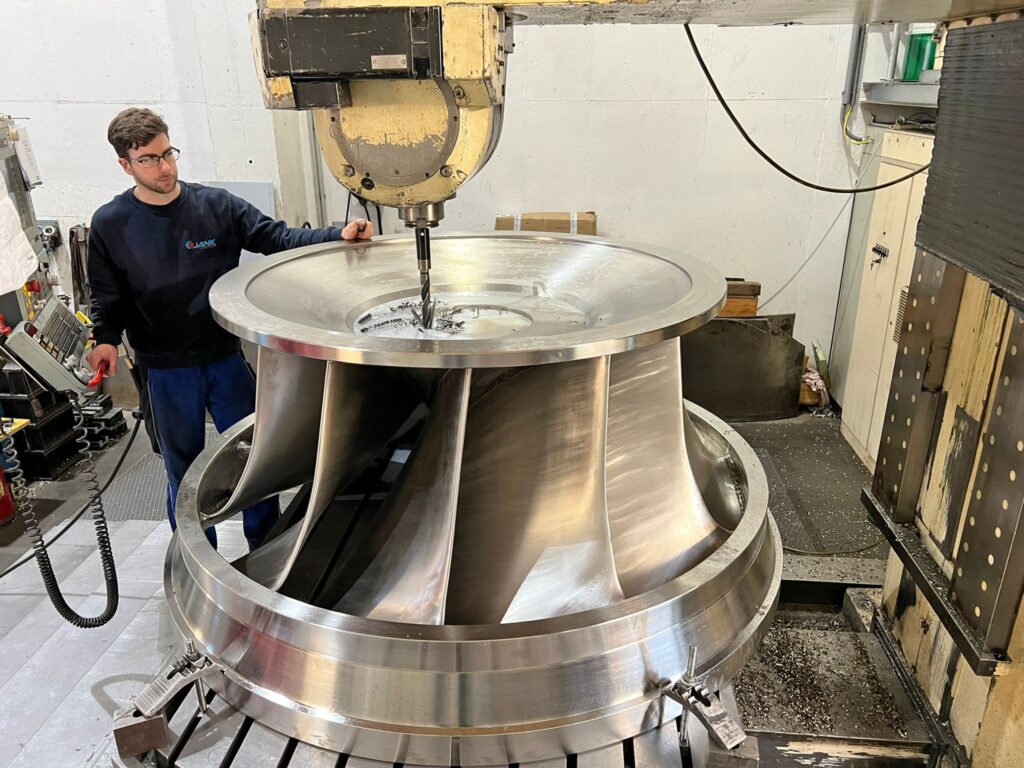 Arbeiter an CNC-Maschine bei der Metallbearbeitung eines großen Turbinenrads in einer Industrie-Werkstatt.