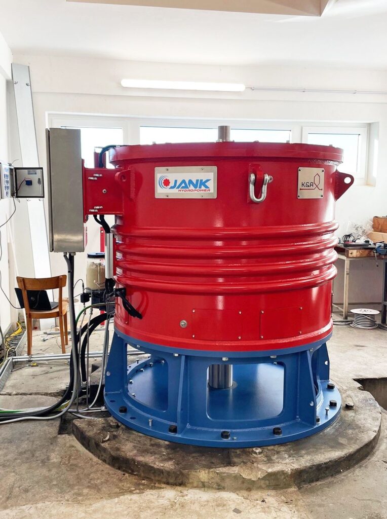 KW Brauhof Generator von Jank Hydropower: Vertikaler rot-blauer Wasserkraft-Generator in einer Industriehalle.