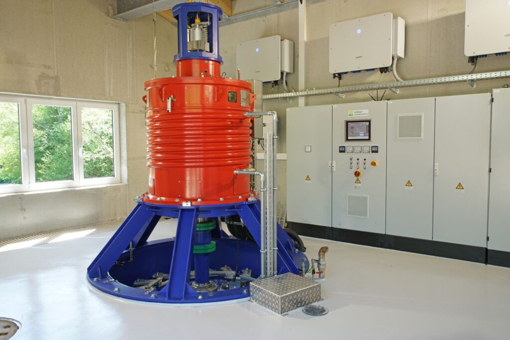 Industrielle Wasserturbine in Rot und Blau im Turbinenraum mit Schaltschränken zur regenerativen Energiegewinnung.