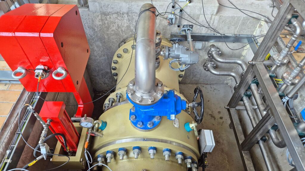 Industrielle Rohrleitung mit blauem Absperrventil, Handrad und Manometer in einer technischen Anlage.
