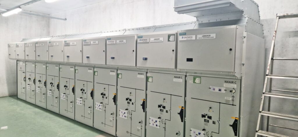 Moderne elektrische Infrastruktur mit einer Reihe grauer Siemens NXAIR C Mittelspannungsschaltanlagen in einem Technikraum.