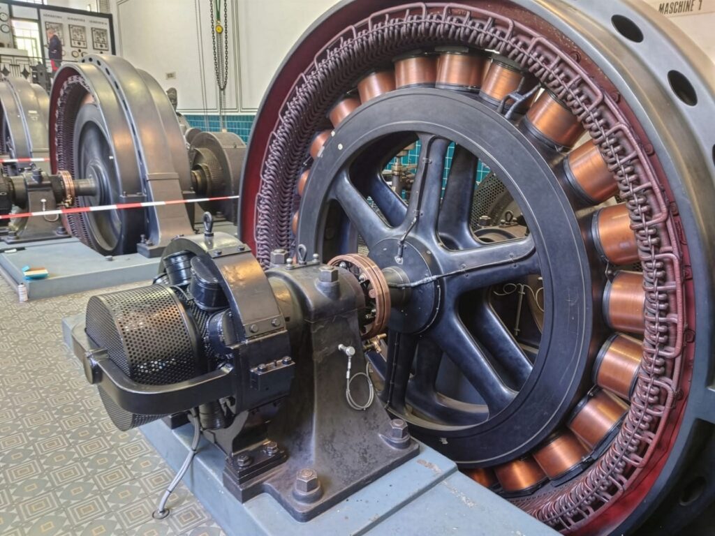 Historischer Generator mit Kupferwicklungen und großem Schwungrad in einem Industriedenkmal.