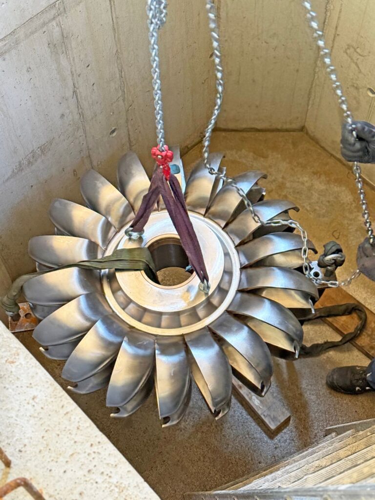 Massives Pelton-Laufrad aus Metall an Hebeketten während der Installation oder Wartung in einem Betonschacht.