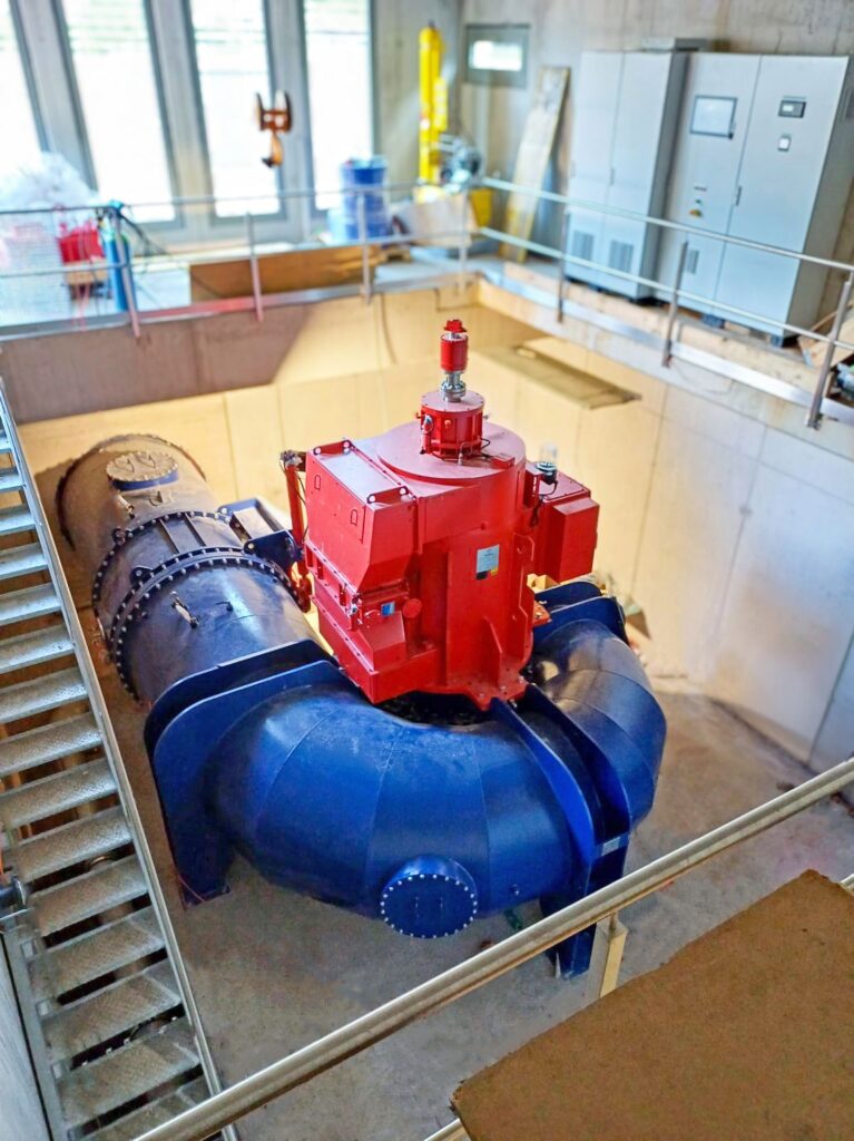 Gugler Wasserturbine in der Hansenhütte mit rotem Generator und blauer Spirale in einem modernen Maschinenraum.