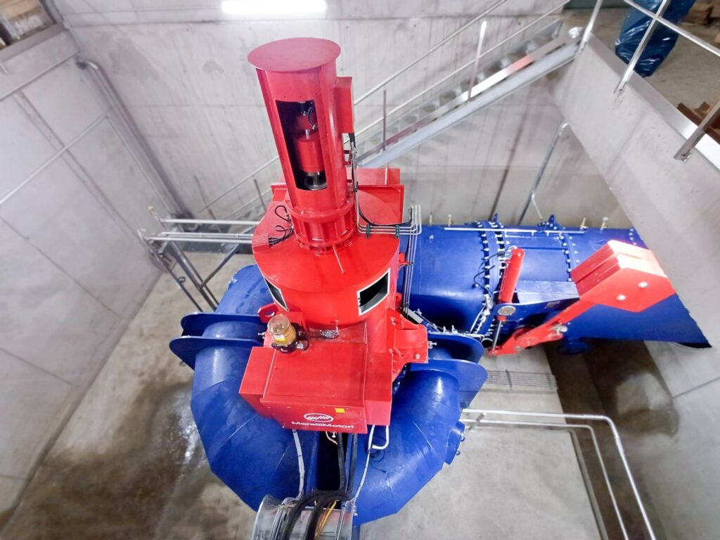 Gugler Wasserturbine mit rotem MarelliMotori Generator in der Hansenhütte, Draufsicht auf blaue Rohrleitungen.