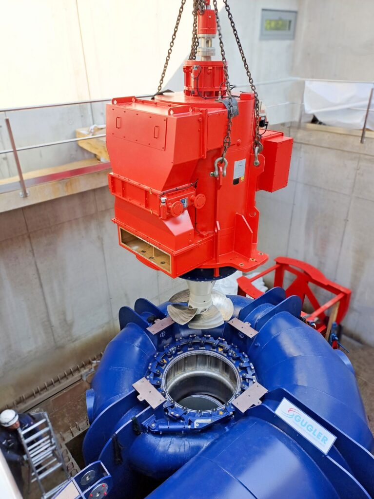 Rote Gugler Wasserturbine wird per Kran in das blaue Gehäuse im Kraftwerk Hansenhütte herabgelassen.