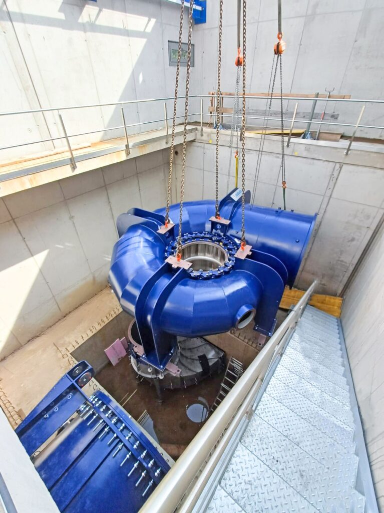 Blaue Gugler Wasserturbine am Kran bei der Montage im Kraftwerk Hansenhütte zwischen Betonwänden.