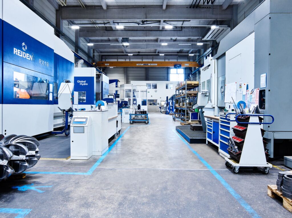 Moderner Maschinenpark von Global Hydro in Österreich mit CNC-Fräsmaschinen und Turbinenbauteilen in einer Industriehalle.