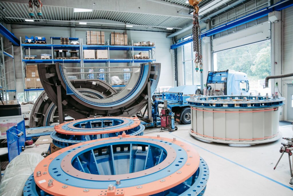 Produktion großer Wasserkraftkomponenten in der Fertigungshalle von Global Hydro in Österreich mit Turbinenteilen und LKW.