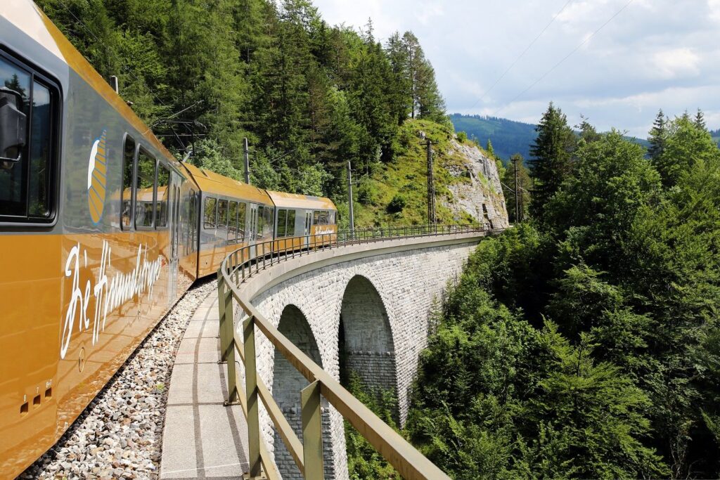 Goldene Himmelstreppe der Mariazellerbahn fährt über ein steinernes Viadukt inmitten grüner Berglandschaft Niederösterreichs.