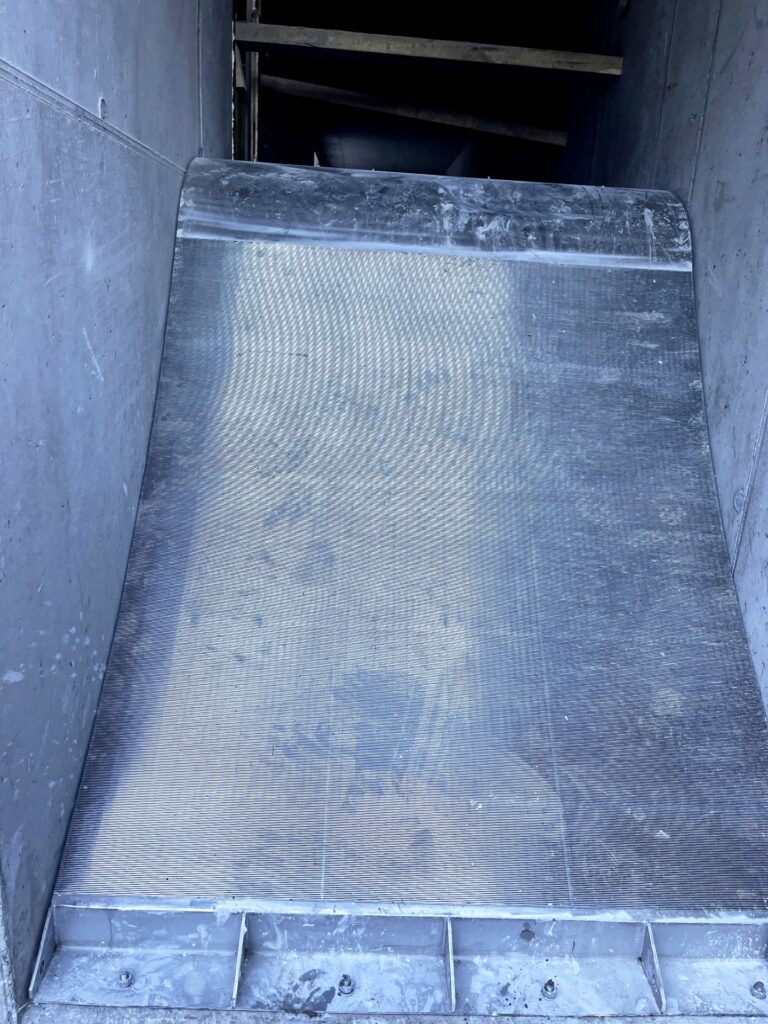 Industrieller Feinspalt-Rechen aus Edelstahl in einem Betonschacht einer Abwasserreinigungsanlage.