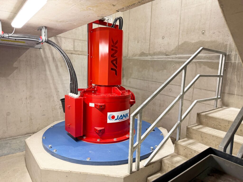 Rote Jank Hydropower Wasserturbine in einem Betonraum mit Treppenaufgang und blauer Bodenplatte.