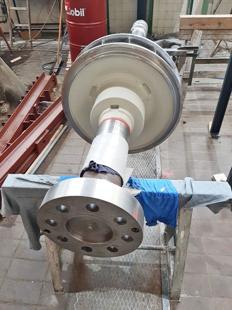 Große Metallwelle vom Kraftwerk Erlaufboden mit Laufrad und Flansch, gelagert auf Böcken in einer Werkstatt.