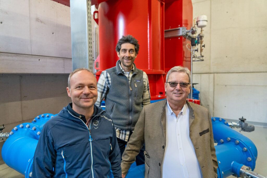 Klaus und Andexer Team bei Gruppenfoto im Kraftwerk vor roter Turbine und blauen Rohrleitungen.