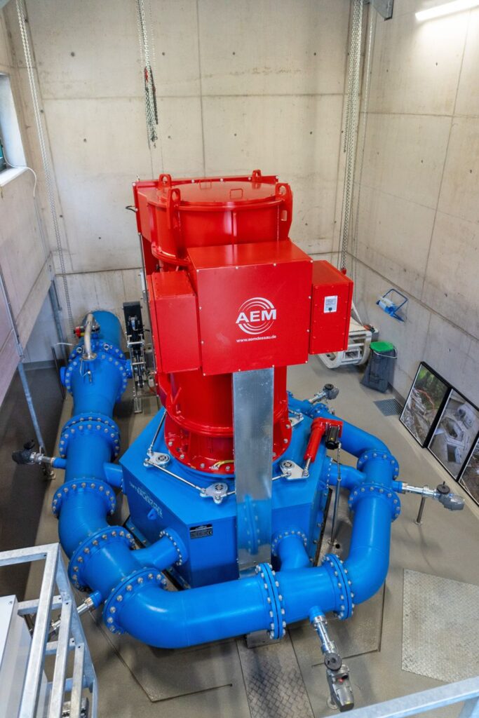Rote AEM Turbine mit blauen Rohrleitungen im Kraftwerk Klaus u. Andexer in einer Betonhalle.