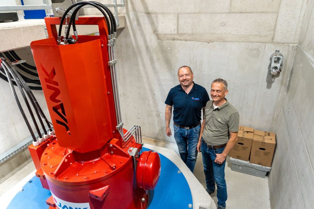 Jank und Sams am Kraftwerk Muntigl neben einer roten Jank-Turbine in einer Industrieanlage mit Betonwänden.