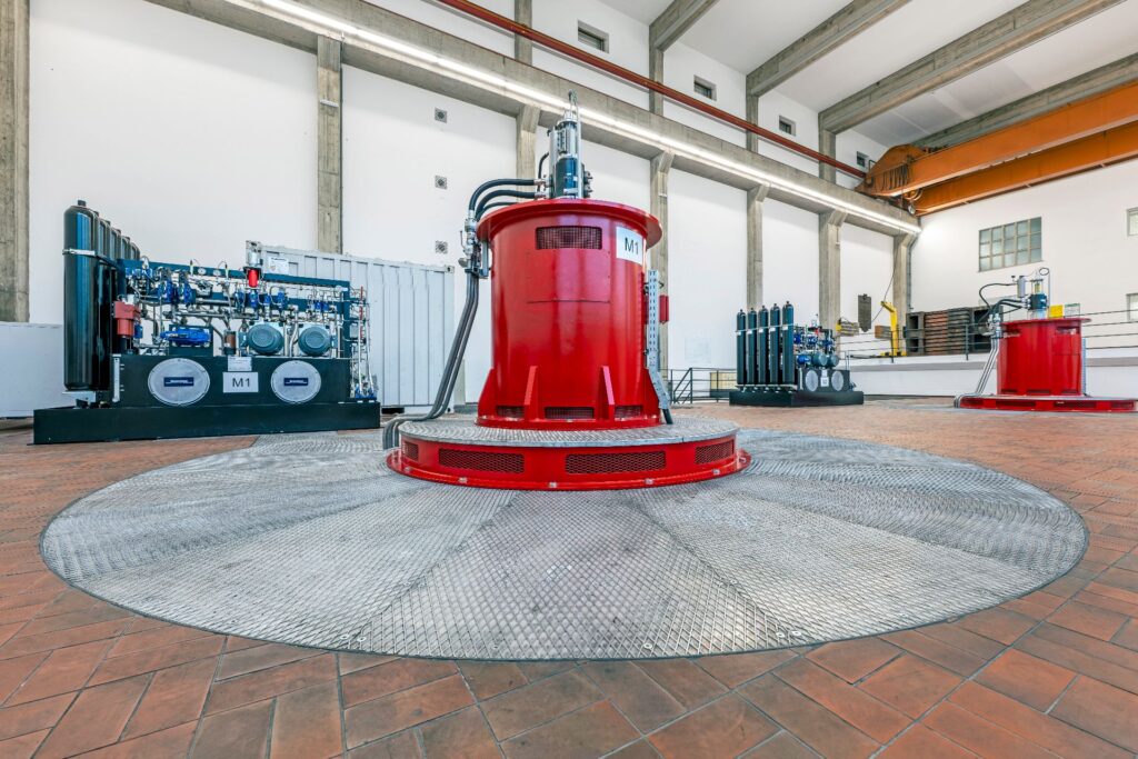 Rote Turbine der Maschinenhalle Kraftwerk Weißhaus auf runder Metallplatte umgeben von technischen Industrieanlagen.