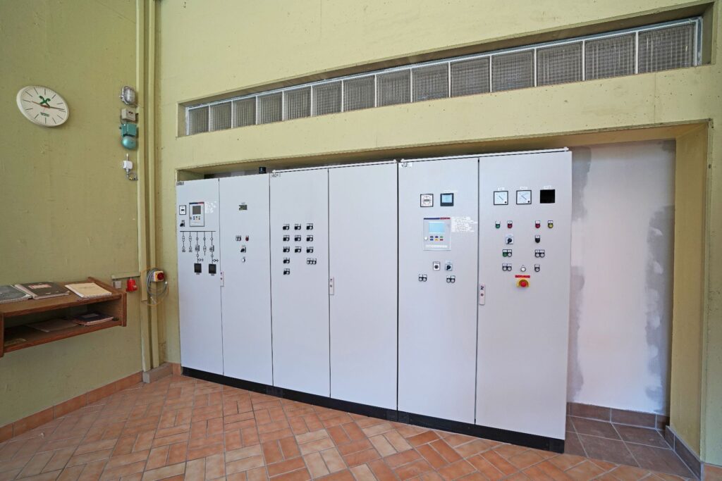 Moderne graue Steuerschränke vom Kraftwerk Möll mit Anzeigen und Schaltern in einem Elektroraum mit Fliesenboden.