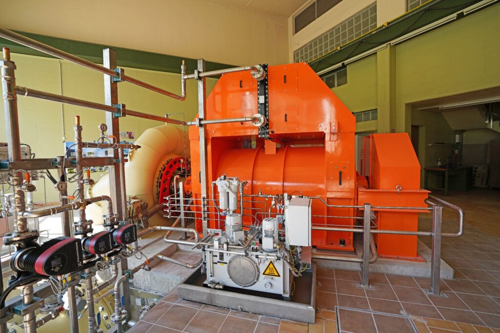 Große orangefarbene Turbine und komplexe Rohrleitungen im Kraftwerk Möllbrücke zur regenerativen Stromerzeugung.