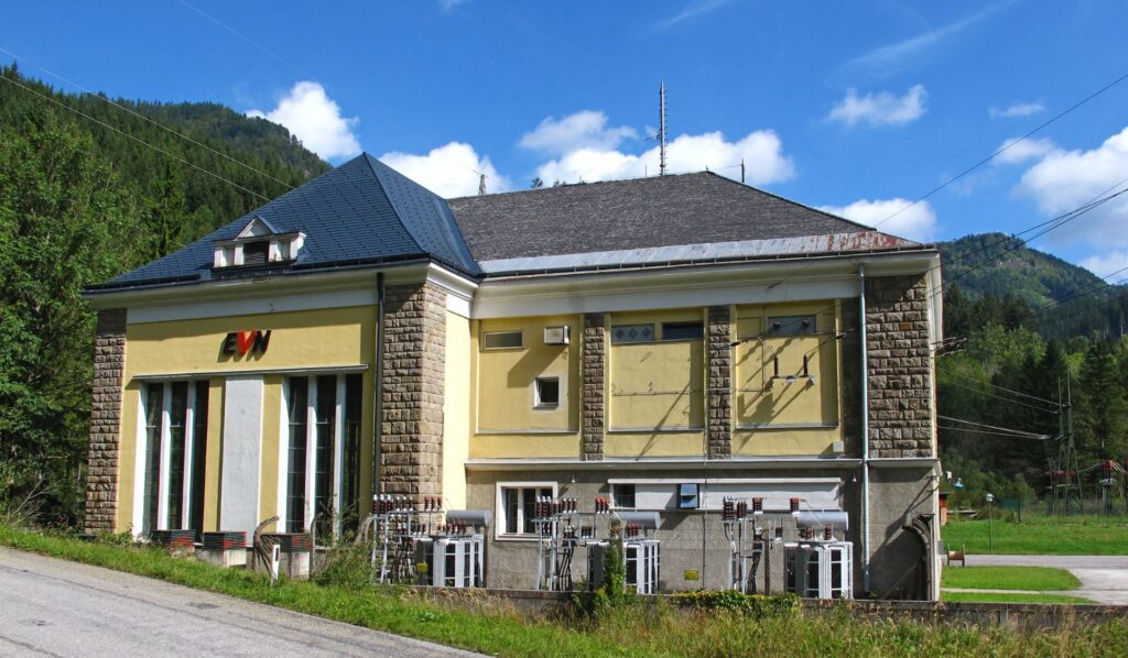 Kraftwerk Erlaufboden der EVN: Gelbes historisches Gebäude mit Schieferdach vor bewaldeten Bergen in Österreich.