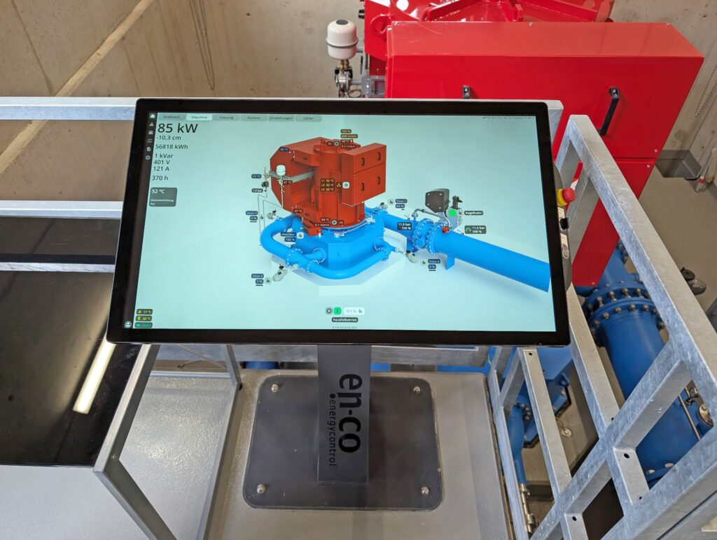 Monitor mit en-co Steuerungssoftware zeigt 3D-Modell einer Industrieanlage mit Leistungsdaten von 85 kW in einem Kraftwerk.