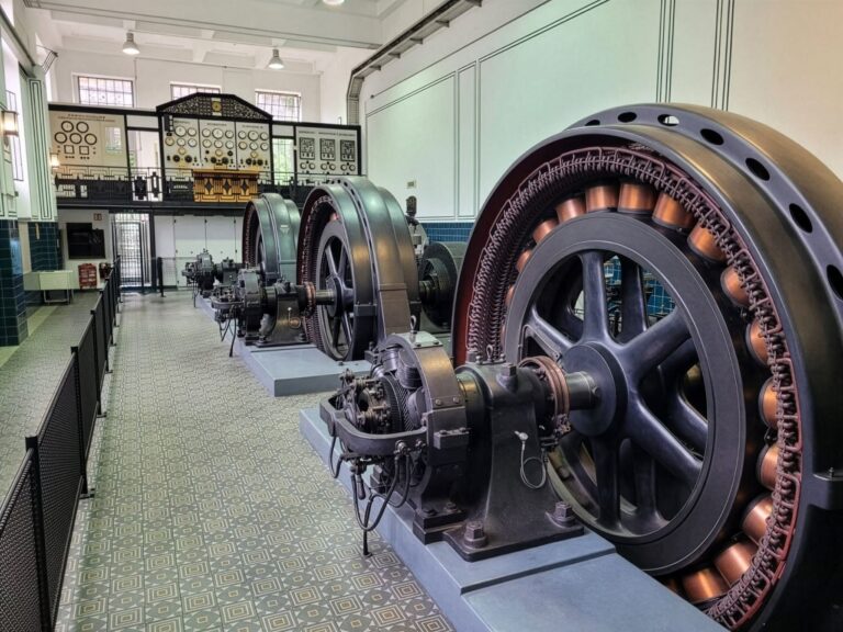Historische Generatoren in einer Maschinenhalle mit Schalttafel im Hintergrund, Industriedenkmal mit Kupferspulen und Fliesen.