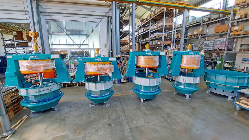Vier türkisfarbene WATEC Hydro Turbinen in einer Industriehalle vor hohen Lagerregalen.