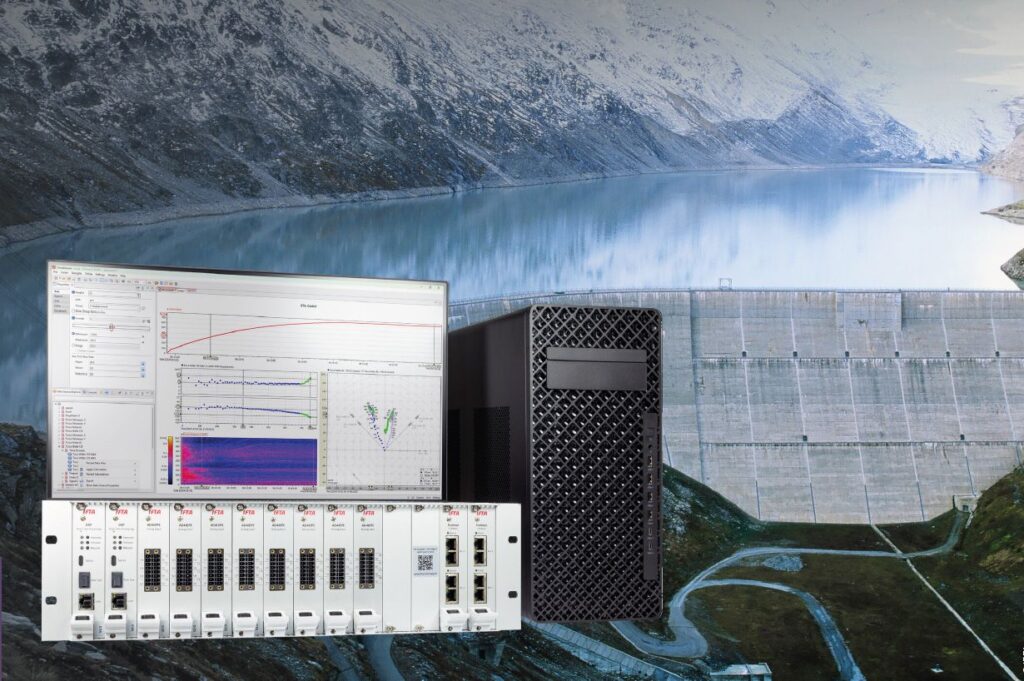 IFTA Messsystem mit Monitor, Server und Hardware-Modulen vor einer Wasserkraft-Staumauer in alpiner Umgebung.