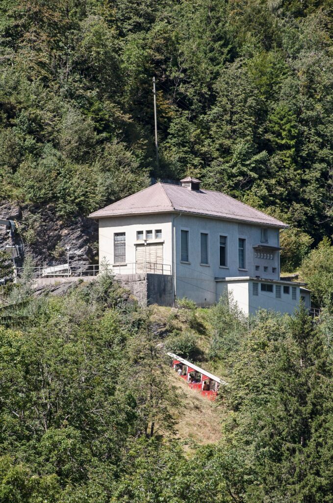 Kraftwerk Schattenhalb 2 mit historischem Gebäude und roter Standseilbahn am bewaldeten Felshang im Berner Oberland.