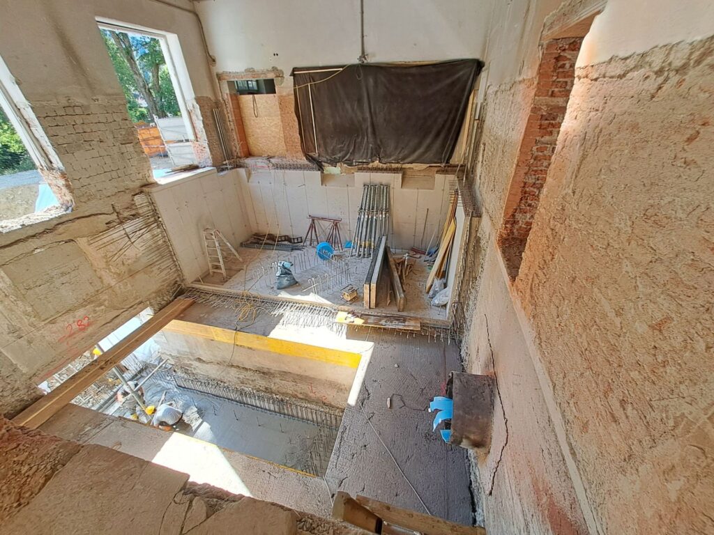 Baustelle im Rohbau mit freigelegten Ziegelwänden, Betonelementen, Stützen und Bewehrungsstahl in einem Altbau.