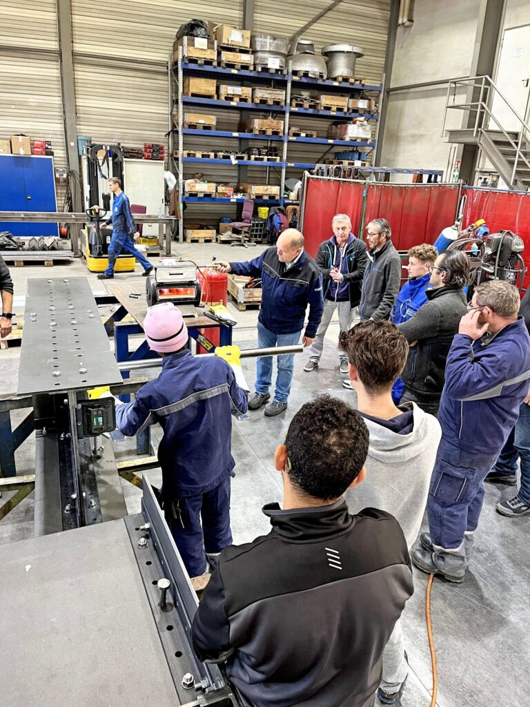Mitarbeiter in einer Industrie-Werkstatt bei einer Einweisung an einem glühenden Härteofen für Metallbauteile.
