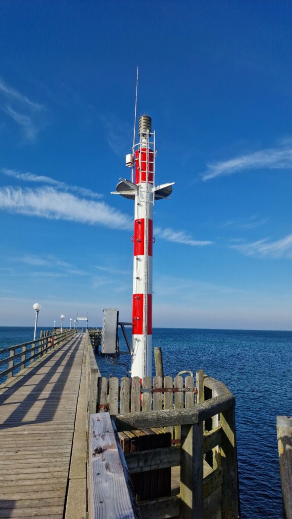 Rot-weißes Leuchtfeuer an einer Seebrücke aus Holz bei blauem Himmel und sonnigem Wetter an der Ostsee.
