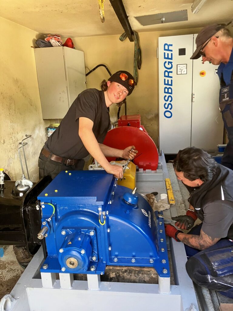 Drei Handwerker bei der Montage einer blauen Ossberger Turbine in einem Technikraum.