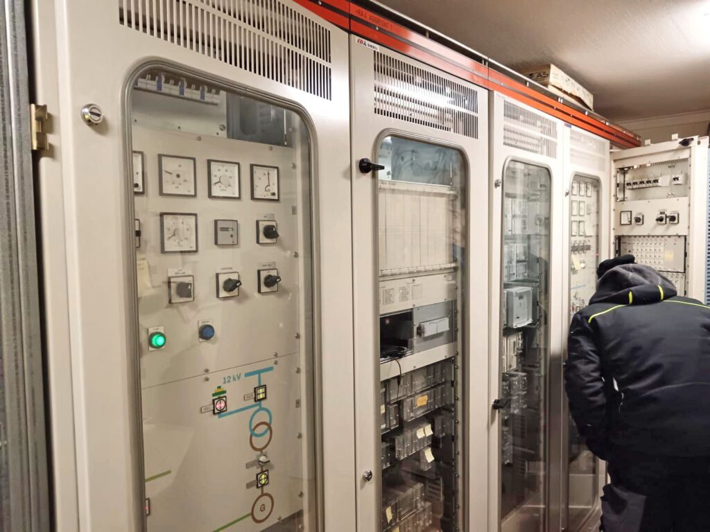 Alter Steuerschrank für 12 kV mit analogen Anzeigen und Drehschaltern, Techniker bei Wartungsarbeiten an der Elektrik.