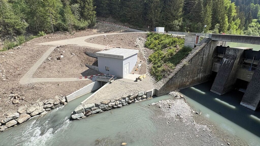 Wasserkraftwerk Burvagn der EWZ: Graues Betriebsgebäude an Staumauer mit Wasserzulauf im bewaldeten Tal.