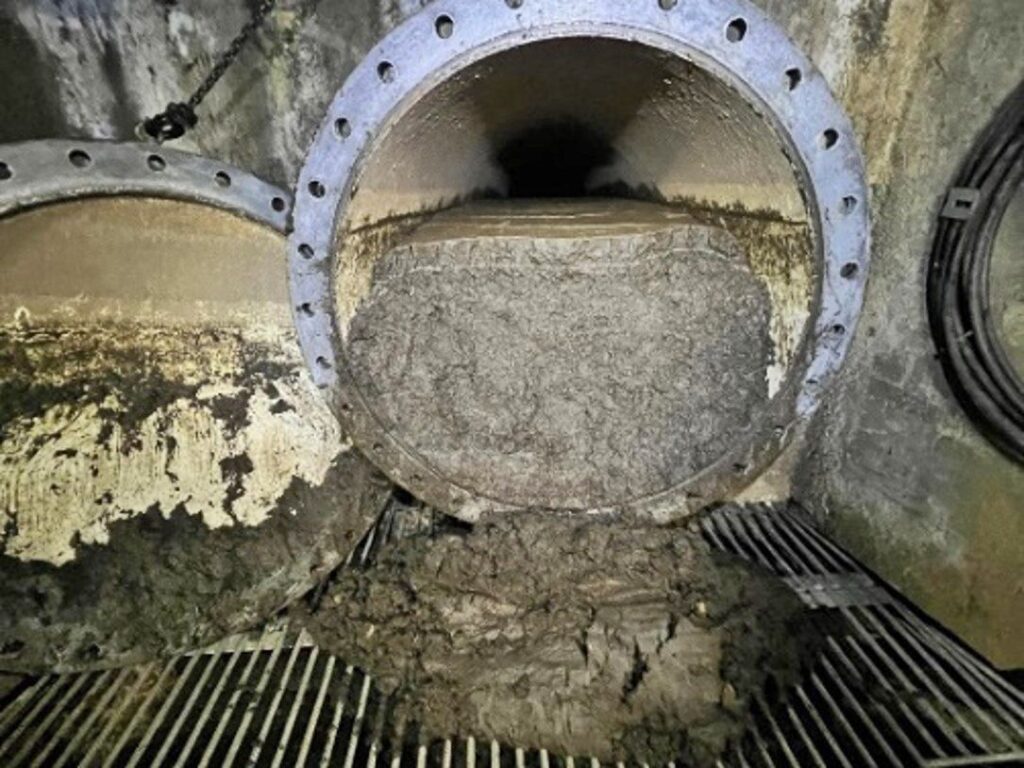 Drosselklappe Grono mit massiver Verstopfung durch graue Ablagerungen in einem geöffneten Metallrohr.