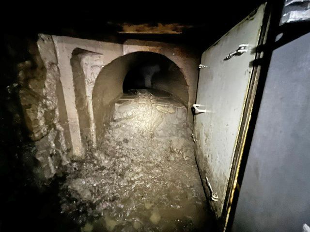 Mit Schlamm und Geröll verstopfte Druckleitung in Grono hinter einer geöffneten Metalltür in einem dunklen Tunnel.