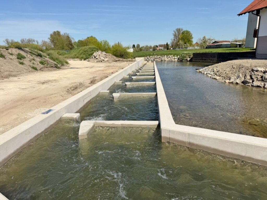 Fischaufstiegshilfe (FAH) aus Beton mit Kaskaden in einem fließenden Gewässer unter blauem Himmel.