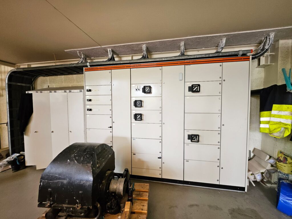 Industrielles AC & DC System mit Schaltschränken, Bedienelementen und einem Elektromotor in einer Werkstatthalle.