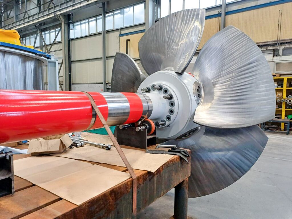 Gugler Kaplan-Turbine für das Wasserkraftwerk Na An mit großen Edelstahlschaufeln und roter Welle in der Montagehalle.