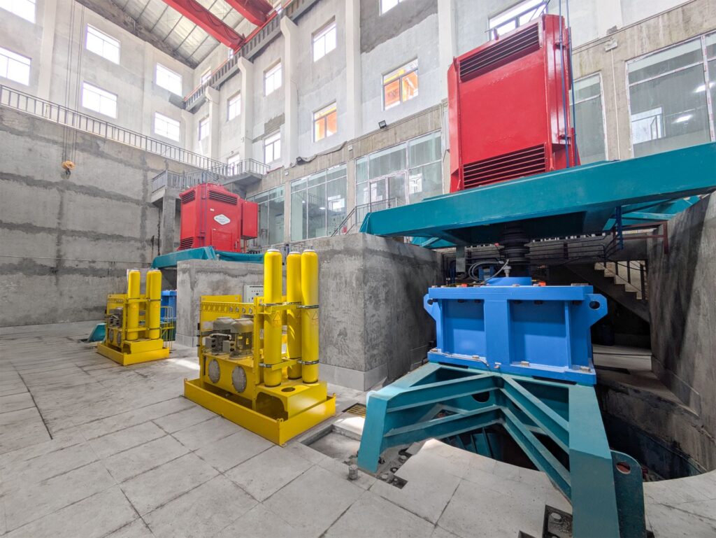 Gugler Wasserkraftanlage Na An mit roten Generatoren und gelben Hydraulikeinheiten in einer Industriehalle.