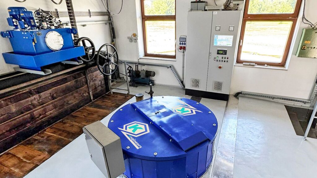 Blauer Generator der KE Bilgram Anlage mit Steuerungsschrank und technischer Mechanik in einem hellen Industrieraum.
