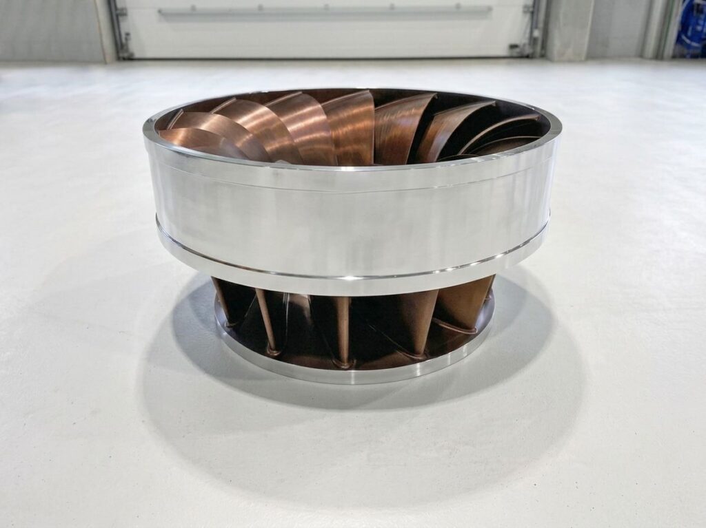 Global Hydro Francis-Laufrad aus glänzendem Metall und Bronze für Wasserkraftanlagen in einer Industriehalle.