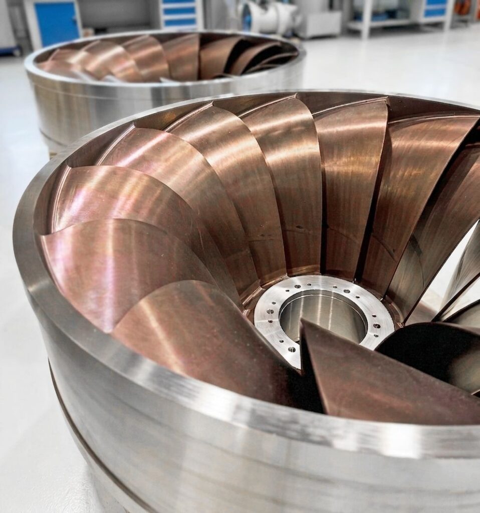 Zwei glänzende Francis-Laufräder aus Bronze und Stahl für Global Hydro Donkea Wasserkraftanlagen in einer Fabrikhalle.