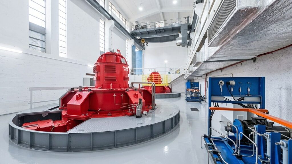 Roter Global Hydro Generator im Donkea Powerhouse. Moderne Wasserkraftanlage mit Industrie-Kran und blauer Steuerungstechnik.