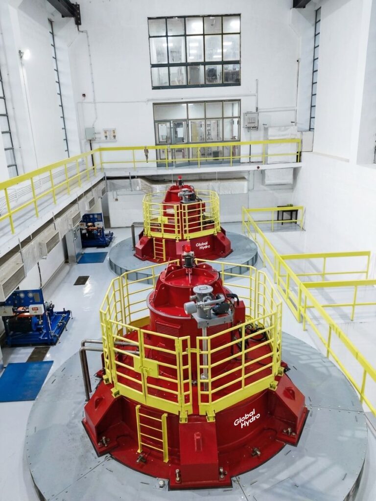Zwei rote Global Hydro Generatoren mit gelben Schutzgittern im hellen Donkea Powerhouse Maschinenraum.