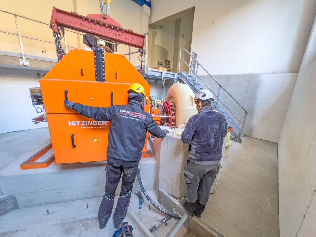 Techniker bei der Montage eines Hitzinger Generators in einem Wasserkraftwerk. Einer trägt Schutzkleidung von SPB Scheiflinger.