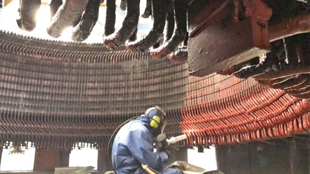 Industrielle Trockeneisreinigung einer Generator-Statorwicklung durch einen Techniker in blauer Schutzkleidung.