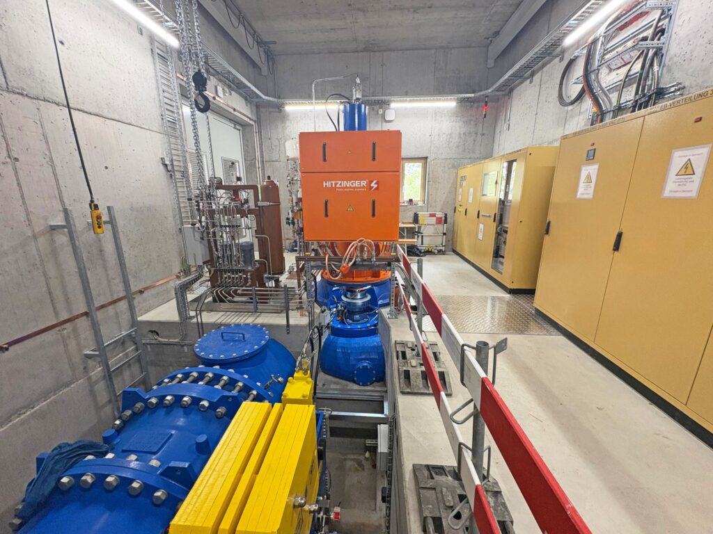 Hitzinger Stromerzeuger in Industriehalle mit blauen Rohrleitungen, Schaltschränken und technischer Infrastruktur.